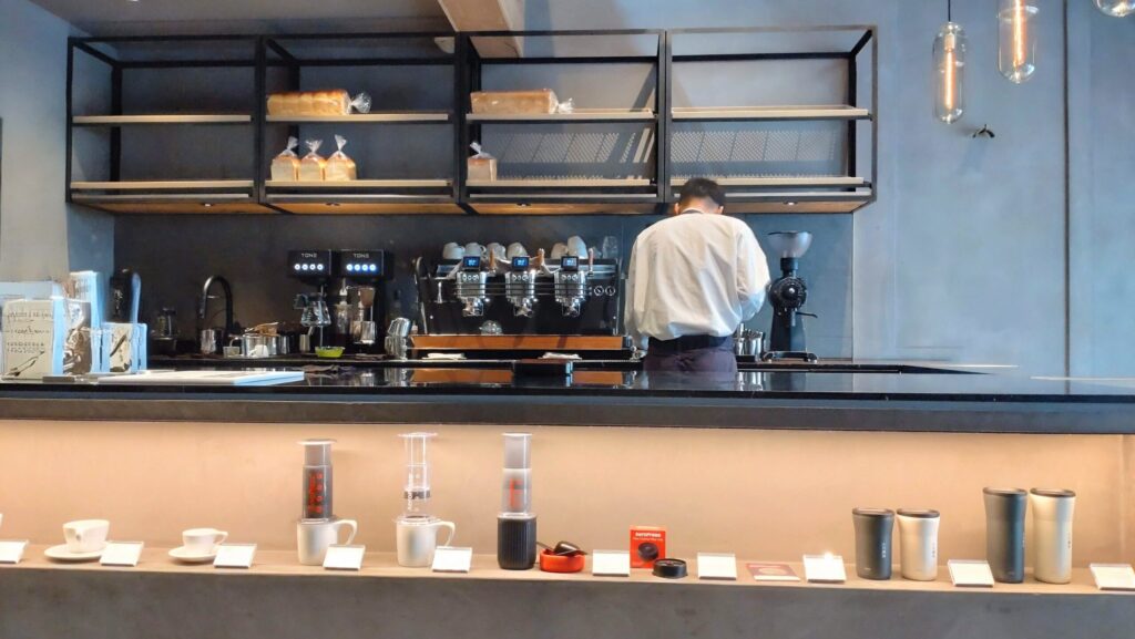 小川珈琲堺町錦店のバリスタカウンターの様子。スタイリッシュな内装の中、バリスタがドリンクを丁寧に準備中。洗練された雰囲気とこだわりの設備が印象的な店内。