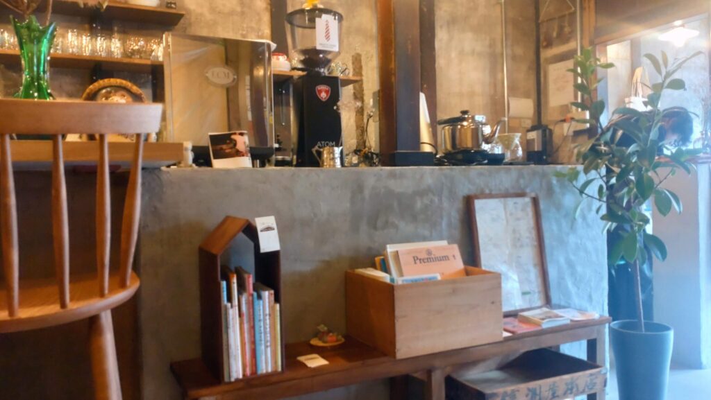 ネクタイコーヒーのカウンター。コーヒー豆を挽く電動ミルや屋根付きの本棚、観葉植物が並び、落ち着いた雰囲気の中に遊び心も感じられる空間。