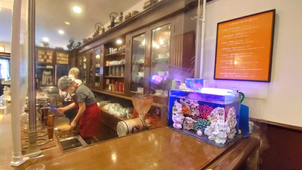 京都・金閣寺近くの珈琲工房の店内。カウンター内ではマスターがコーヒーを手際よく淹れ、奥には水槽がある落ち着いた空間。